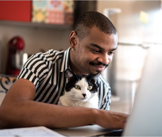 Uomo che usa un computer portatile tenendo in braccio un gatto