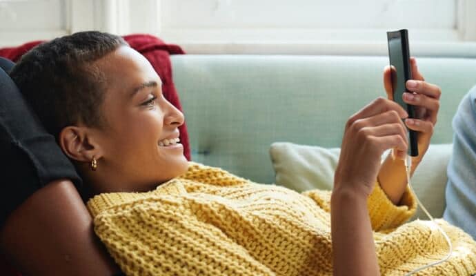 Donna sul divano che osserva il cellulare mentre viene avviato Norton 360 con AntiVirus Plus.