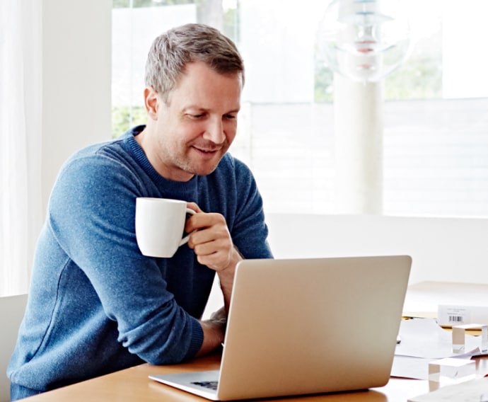 Uomo a casa che utilizza un computer portatile e beve un caffè.