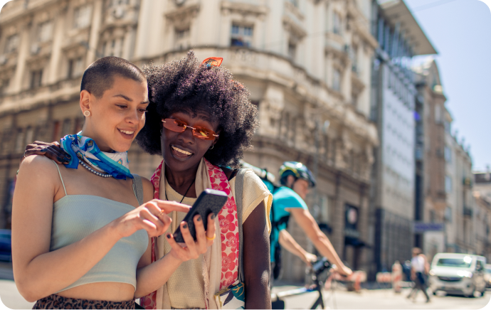 Due donne sorridono e guardano insieme un telefono